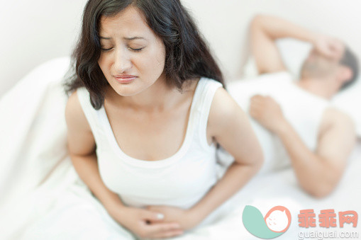 人,睡衣,床,室内,25岁到29岁_476278396_Grimacing woman holding her aching stomach and unaware husband sleeping._创意图片_Getty Images China