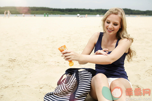 奶油,人,休闲装,包,度假_525469737_Smiling young woman sitting on the beach using suncream_创意图片_Getty Images China