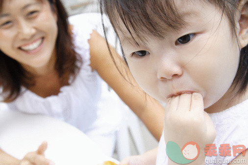 人,衣服,生活方式,户外,人的头部_88797003_Close-up of a baby girl with fingers in mouth and her mother smiling in the background_创意图片_Getty Images China