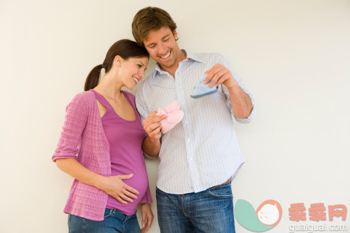 人,人生大事,四分之三身长,室内,快乐_80609563_Young couple, man showing pregnant woman baby slippers, smiling, close-up_创意图片_Getty Images China